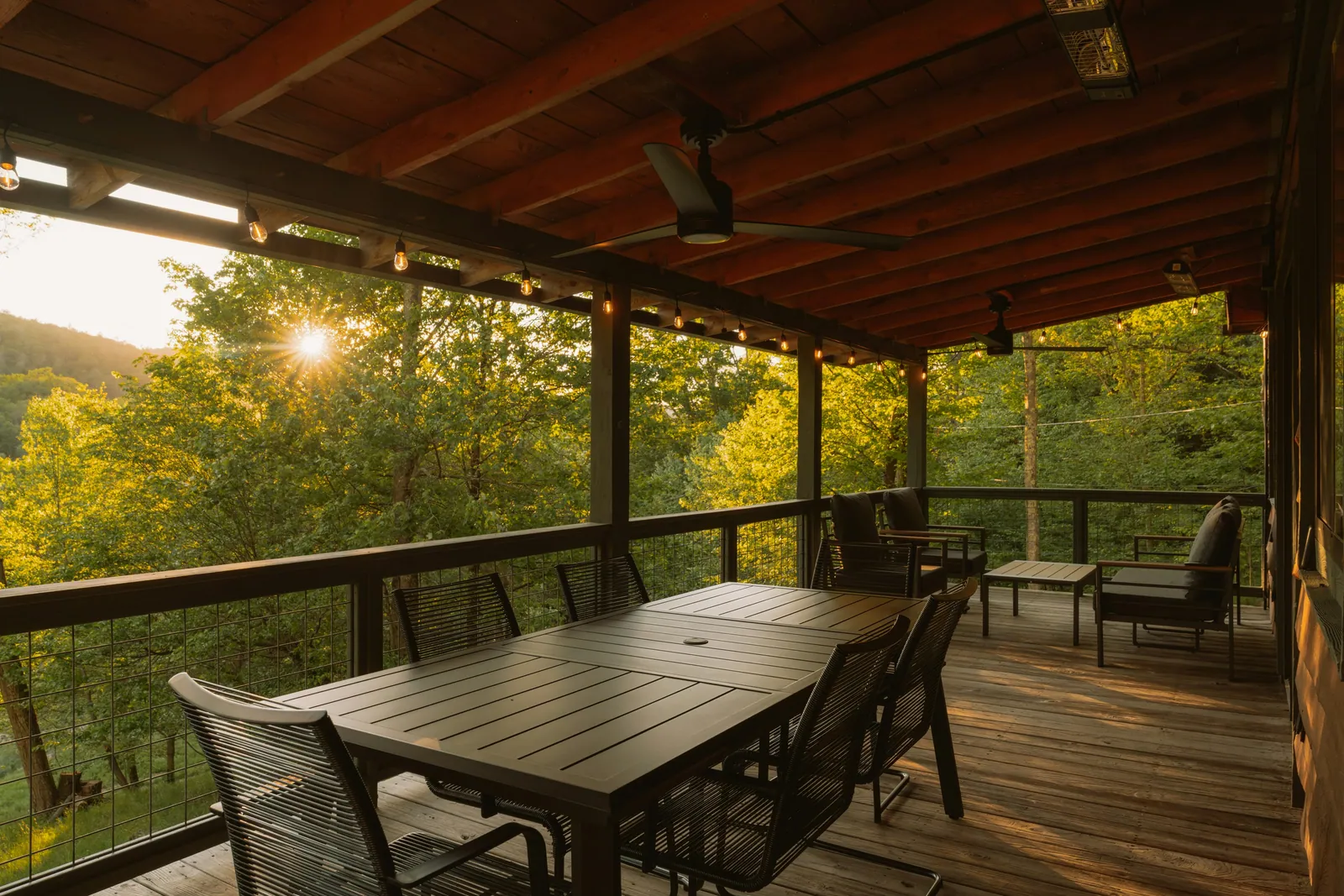 A covered backyard deck at golden hour with a dining table, string lights, and a wooded Nashville view